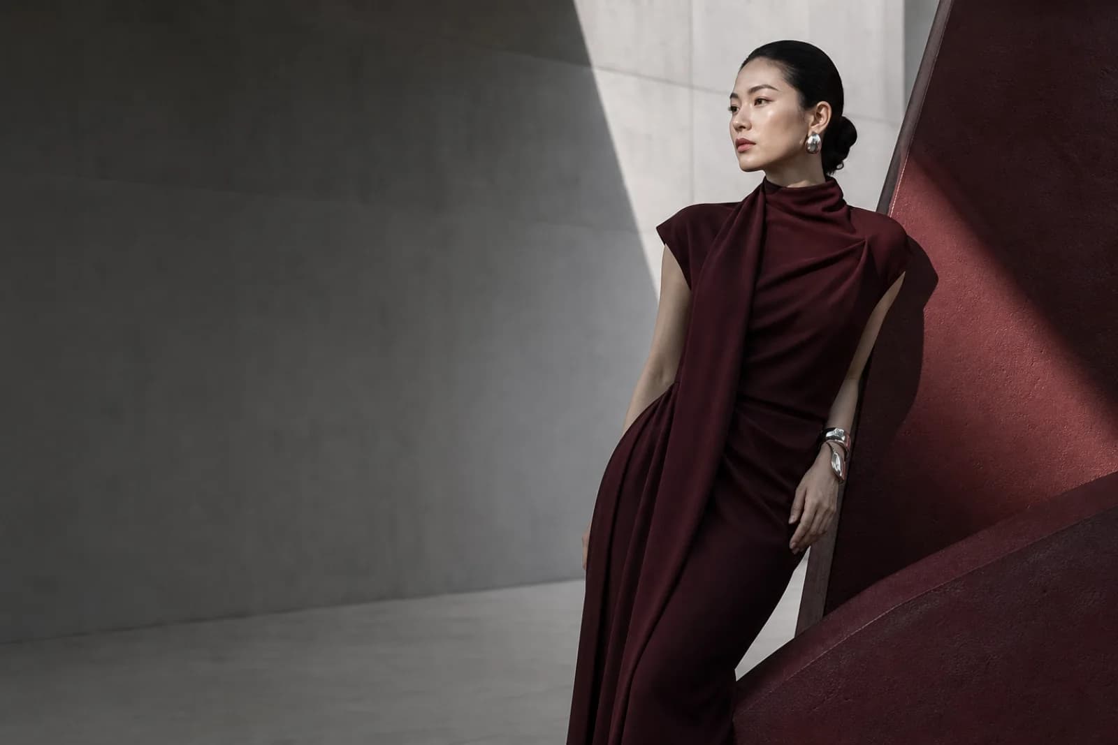 身着酒红色礼服的成年女性站在银灰与酒红建筑空间中